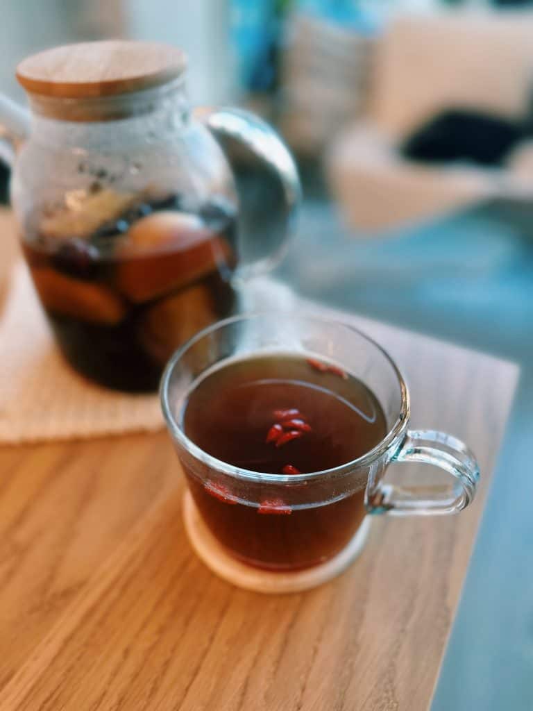 A cup of Apple Herbal Tea with a full pitcher in the background